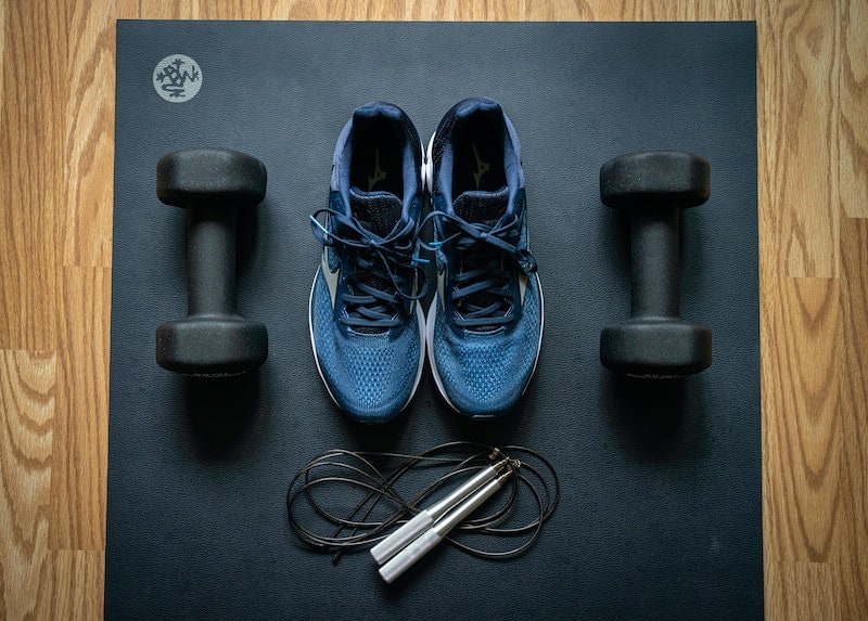 pair of running shoes with a jumprope and handweights next to it on a yoga mat