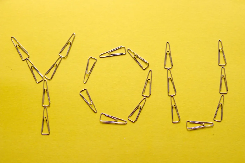 A yellow background with silver paperclips that spell out the word "You"