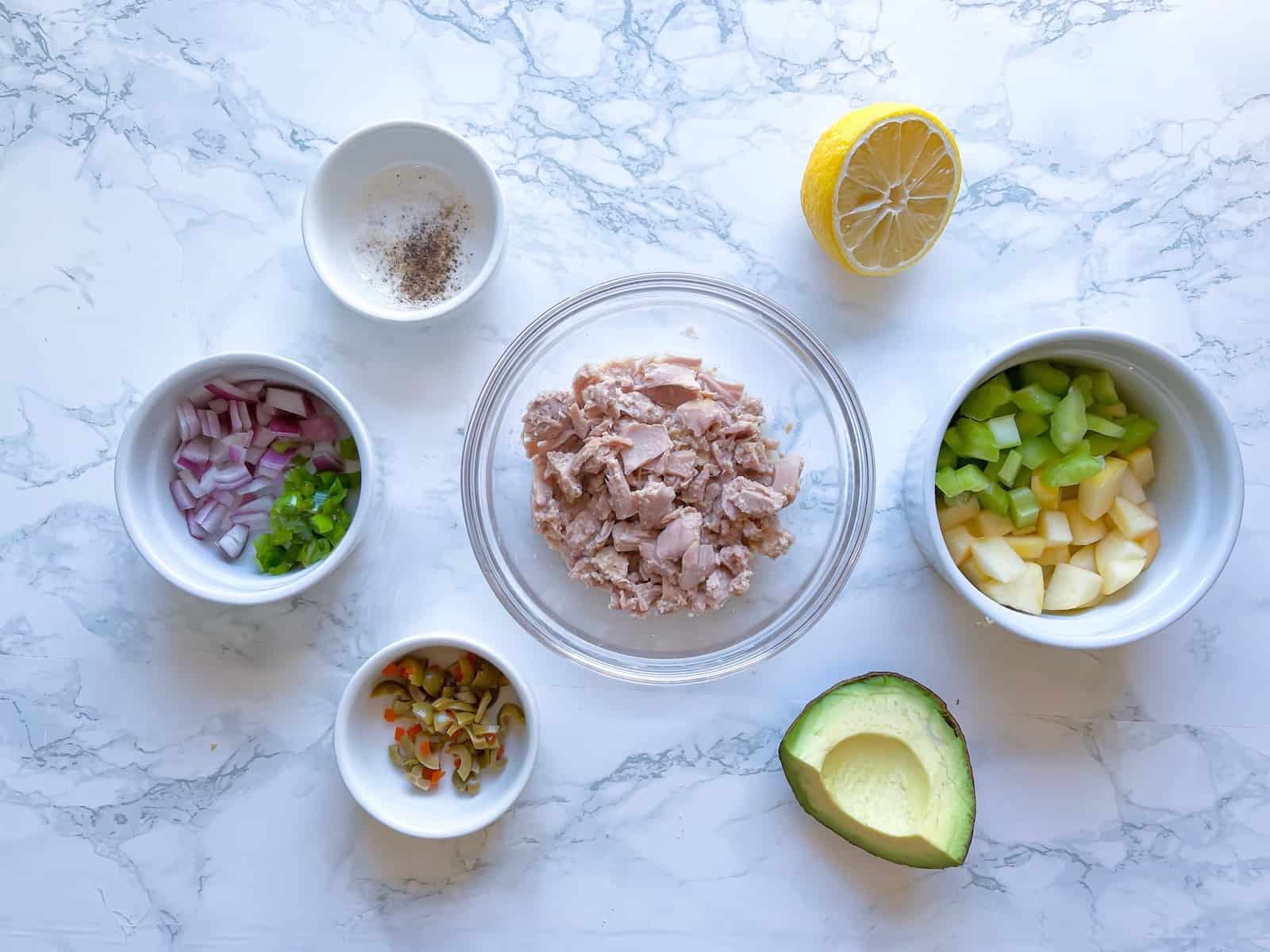 Ingredients for tuna salad without mayo in small bowls on a marble table