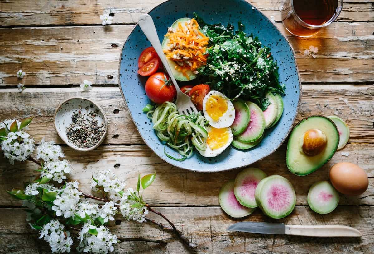 a hormone balancing breakfast including a bowl of egg, greens, avocado and tomato with flowers in the background and a wooden table