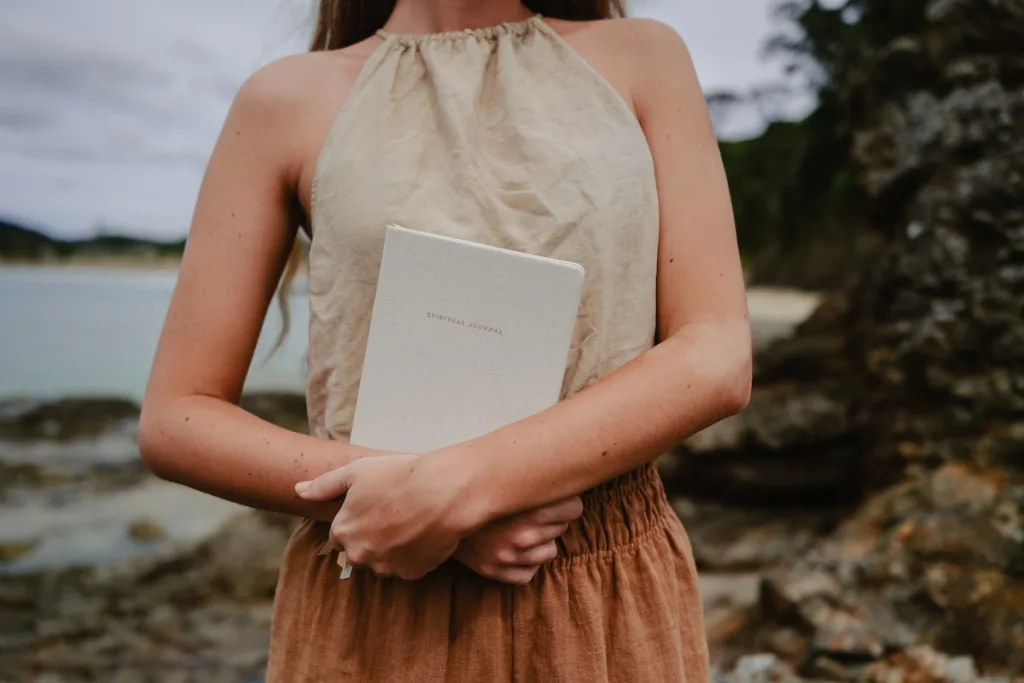 A woman standing a holding a gratitude journal thinking about the 10 benefits of gratitude.