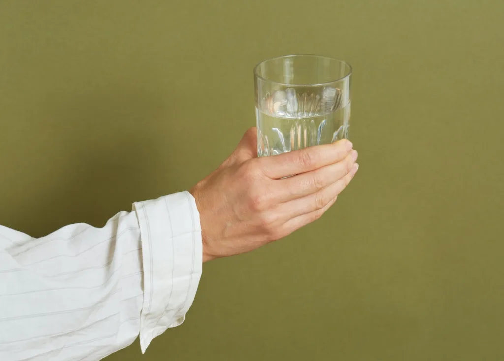 A hand holding a glass of water with an olive green background