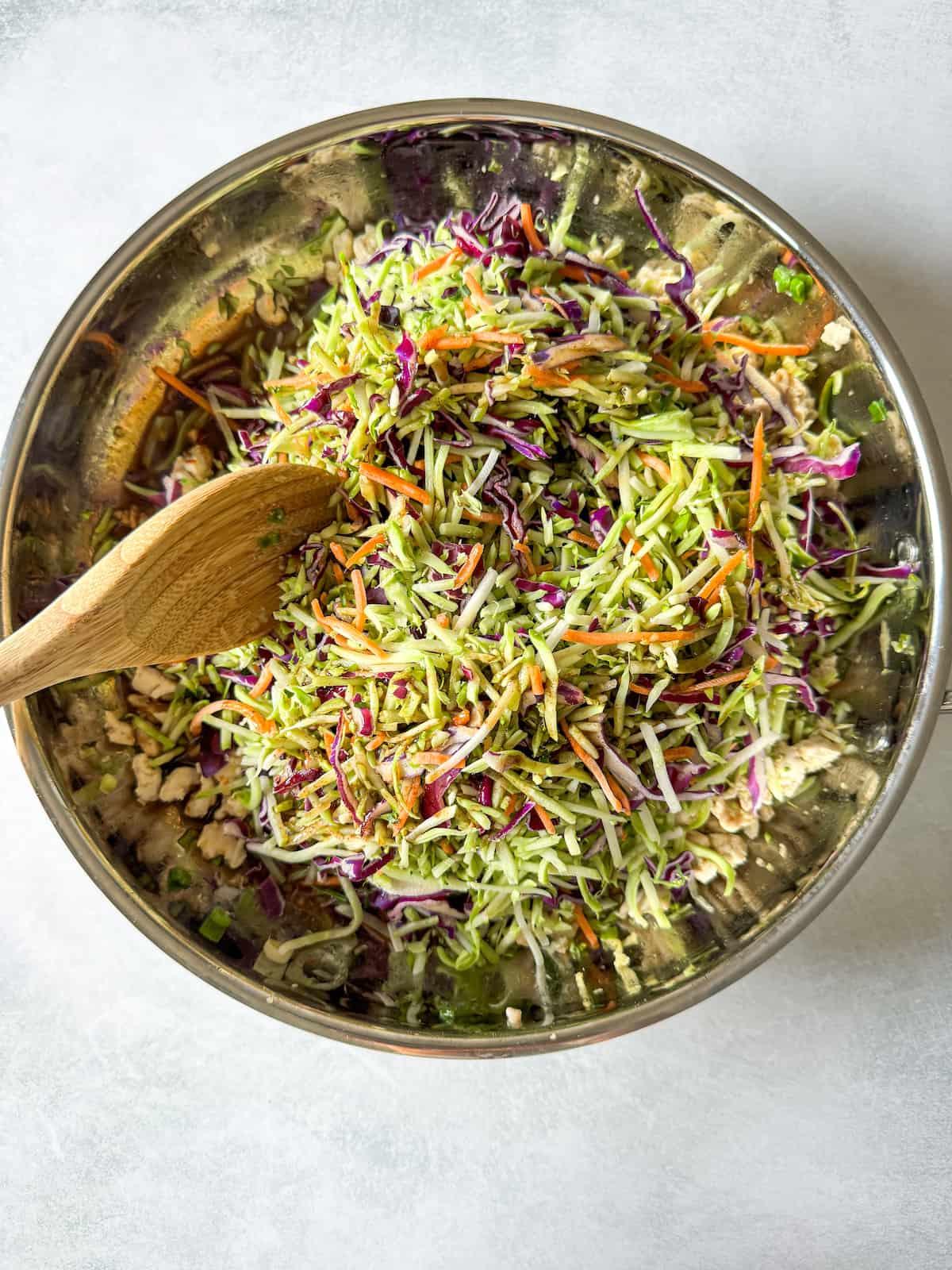broccoli slaw on top of ground turkey with a wooden spoon mixing it all together in a skillet.