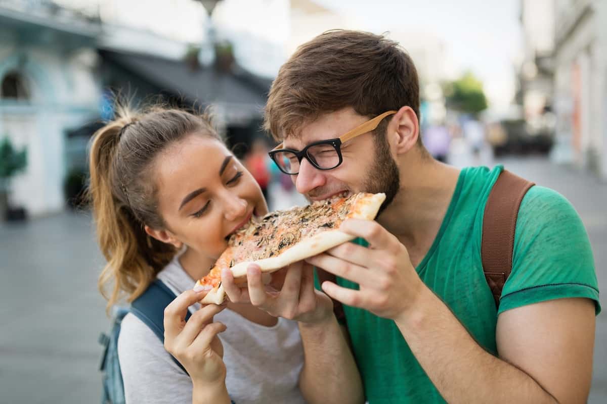 A man and woman eating a pizza. They are both taking a bite at the same time and intuitive eating together.