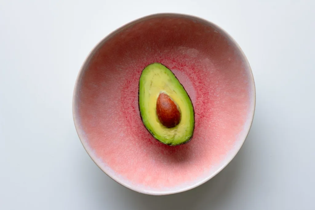 A green avocado in a pink bowl.