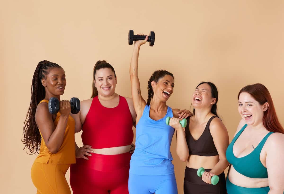 A group of women of all sizes and shapes in workout clothes laughing