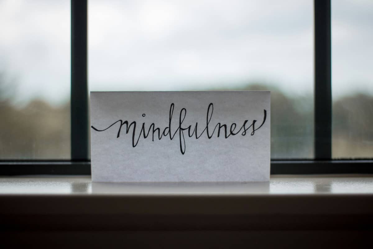 A white paper that says "mindfulness" in black letters with a window in the background