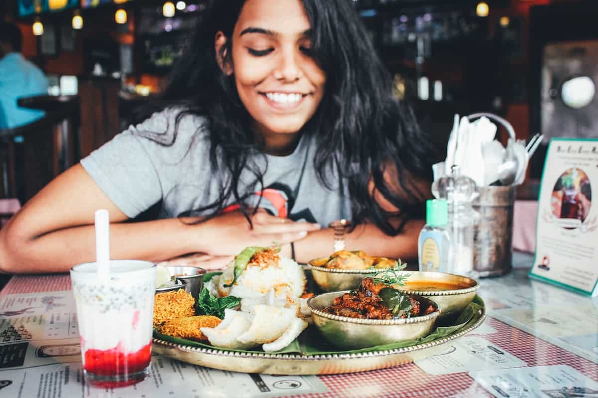 A woman at a restaurant and looking at a plate smiling. She is practices intuitive eating
