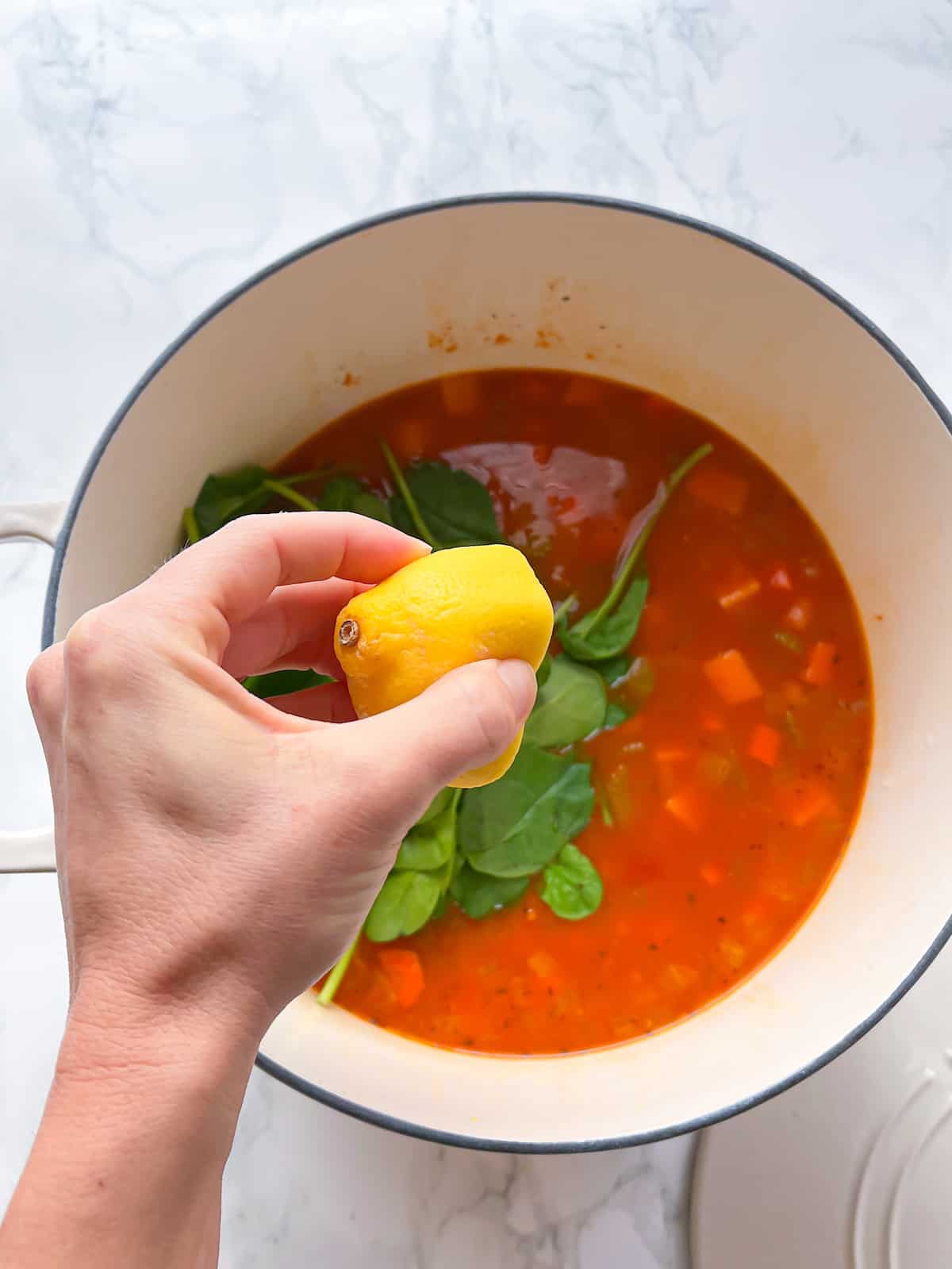 A hand squeezing lemon in vegan chickpea soup
