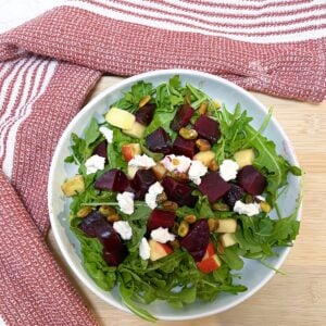 Beet and Arugula salad with goat cheese in a white bowl with a red and white dishcloth in the background