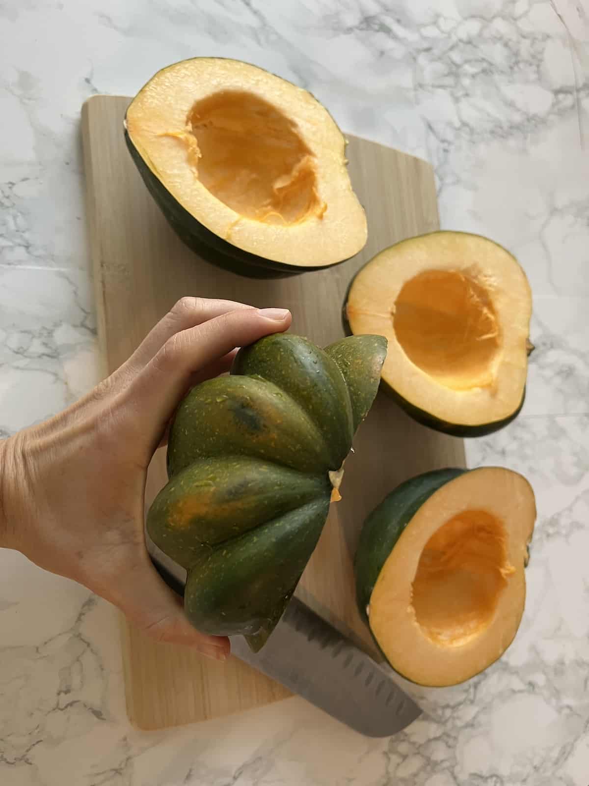 An hand holding half of an acorn squash that has been cut from top to bottom
