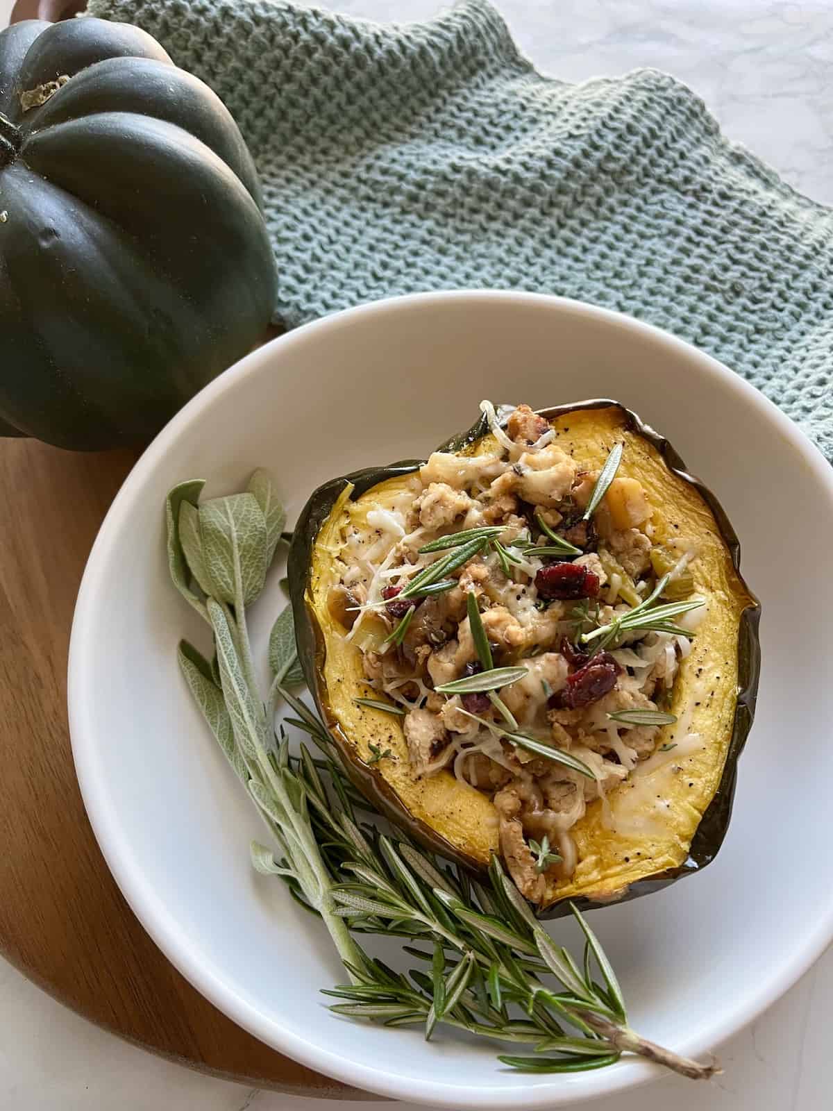The finished product of Ground Turkey Stuffed Acorn Squash in a shallow white bowl with some fresh sage and a green dishcloth in the background