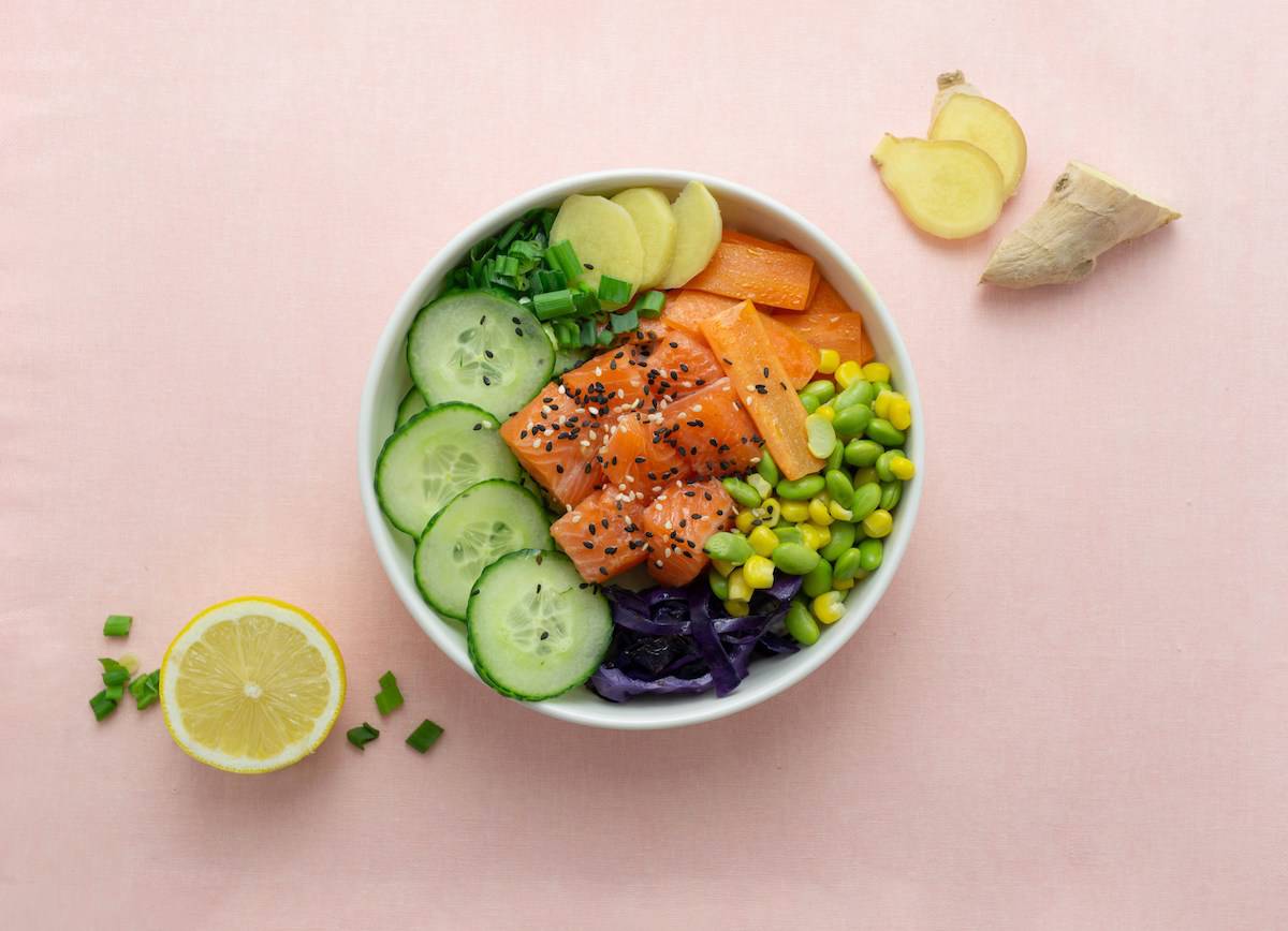 a poke bowl with salmon, edamame, and cucumber slices on a pink background