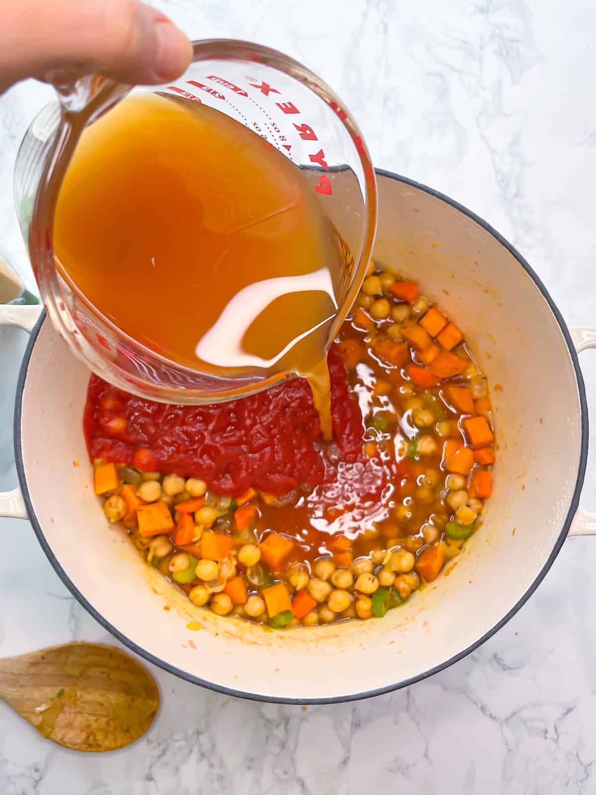 Vegetable broth being poured into vegan chickpea soup over tomato sauce