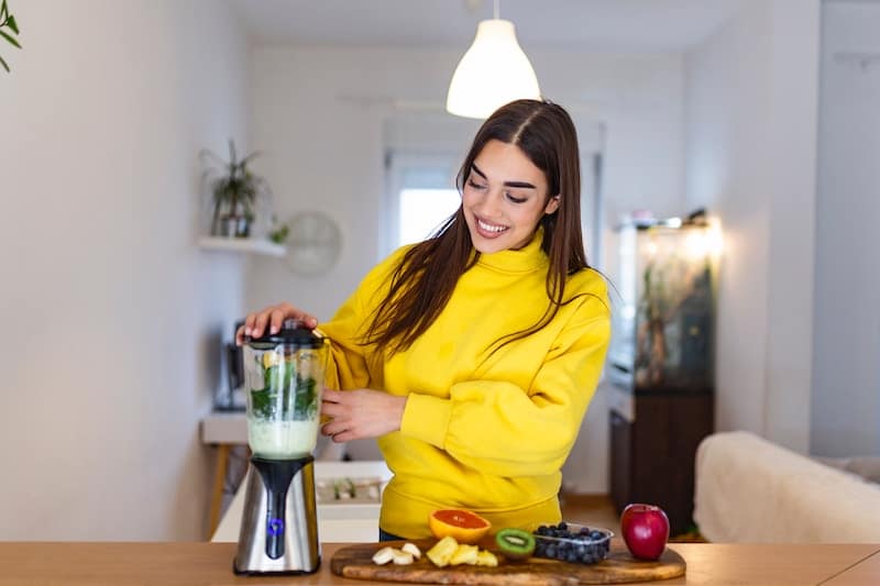 A woman in a yellow sweater making a smoothie with hormone balancing foods like fruits