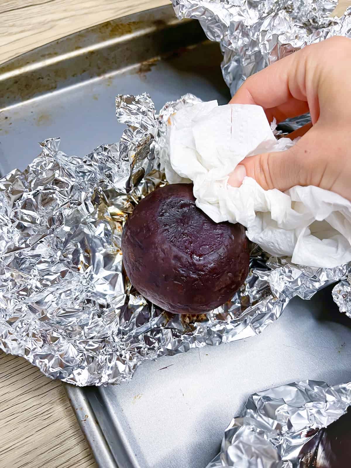 A hand holding a paper towel to take the skin off of roasted beets in foil