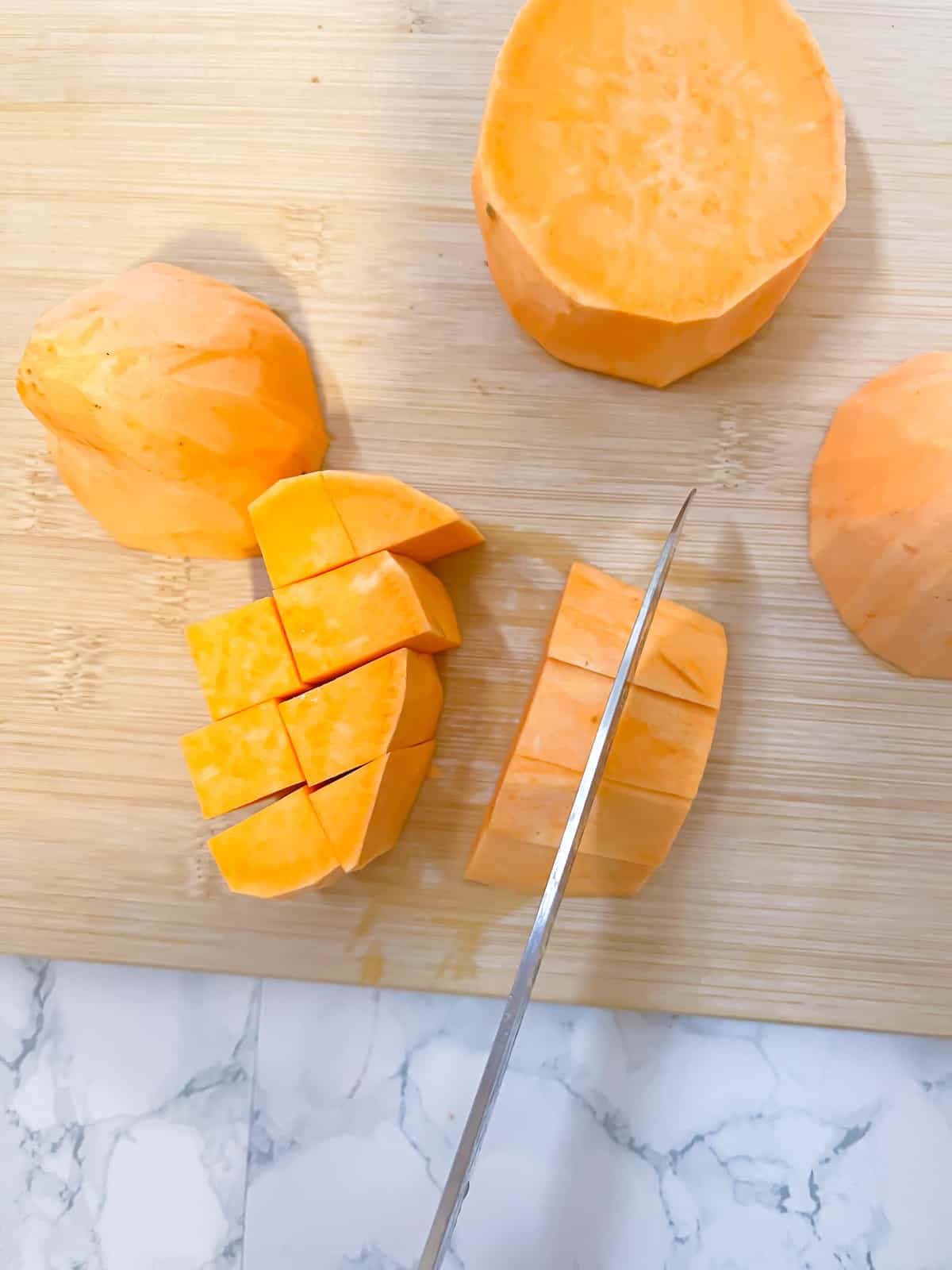 A knife cutting a sweet potato into cubes