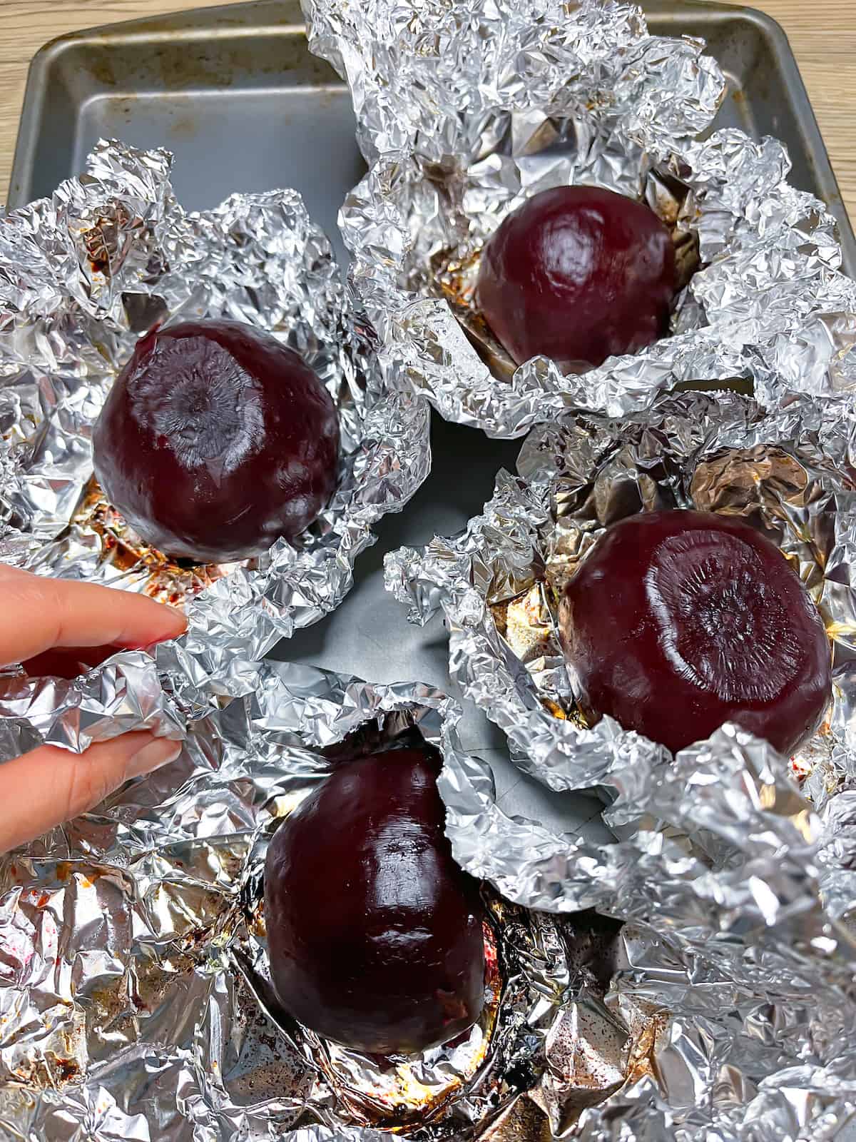 Beets fresh out of the oven still in foil with a hand opening the foil on one of them