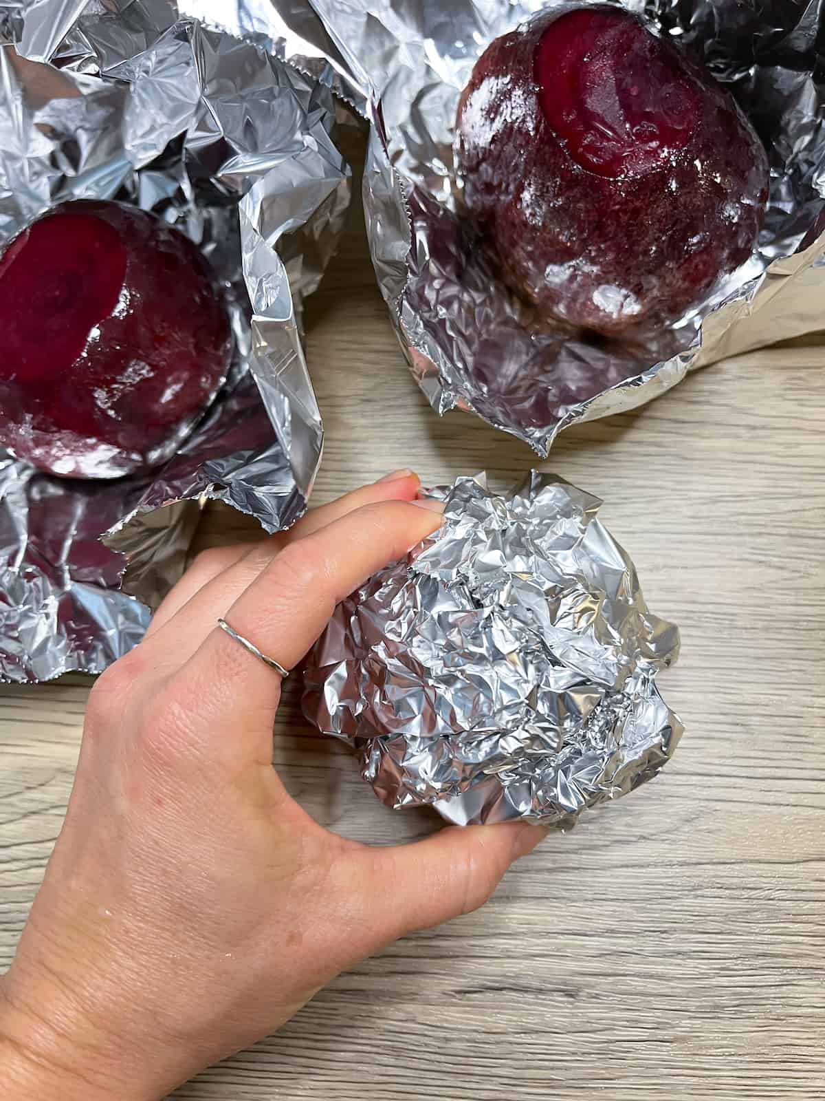 Red Beets wrapped in foil and coated in oil with a hand holding one of the beets