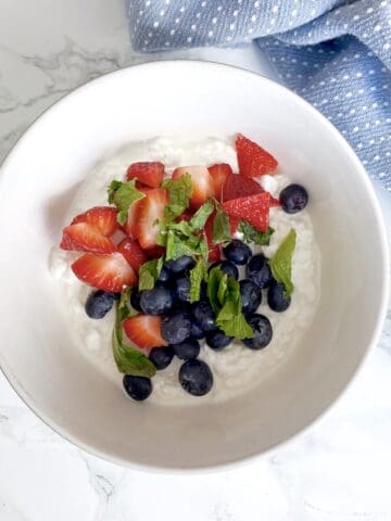 Cottage cheese in a white bowl with strawberries and blueberries on top and mint and honey