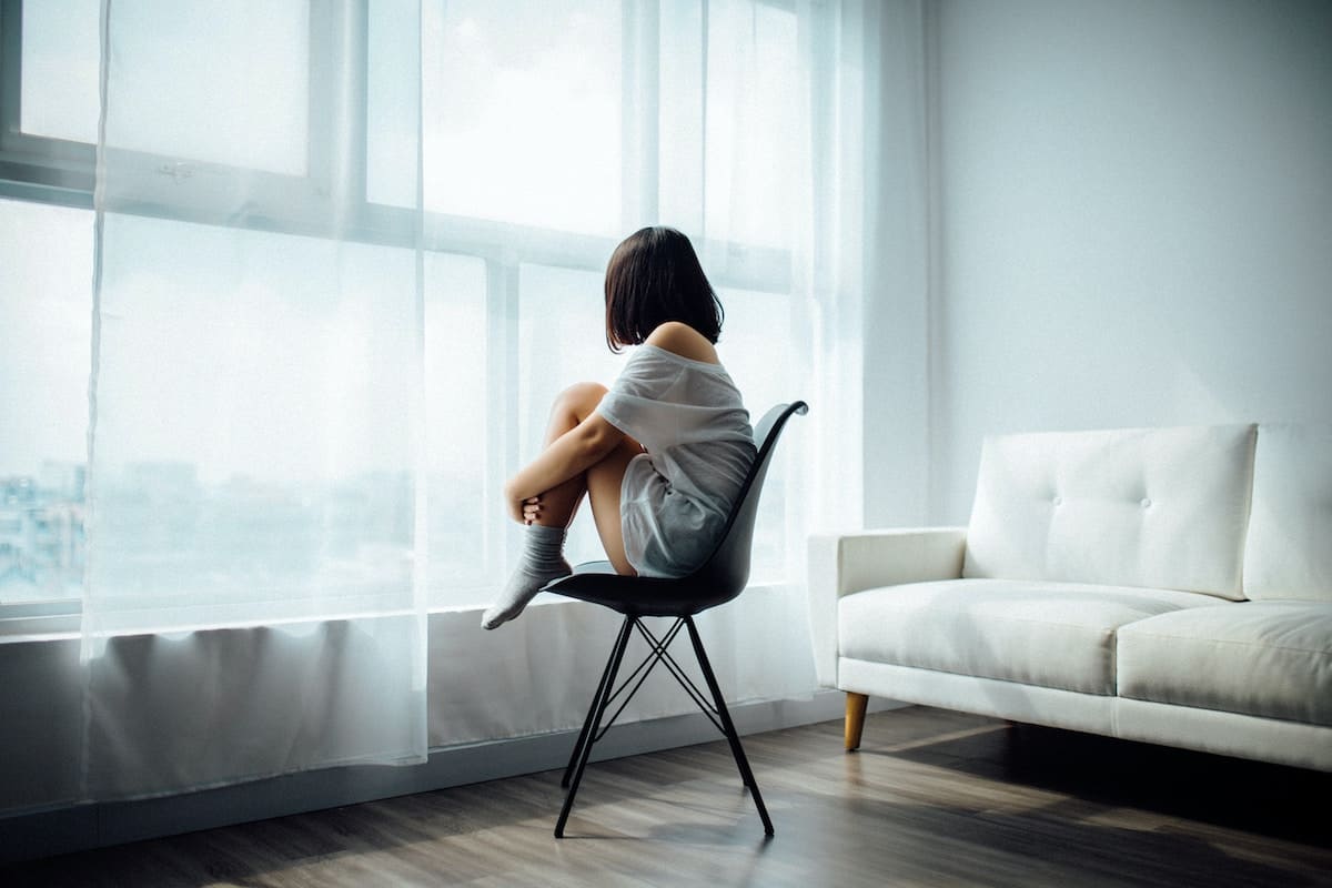 A woman sitting by a window in a chair looking sad