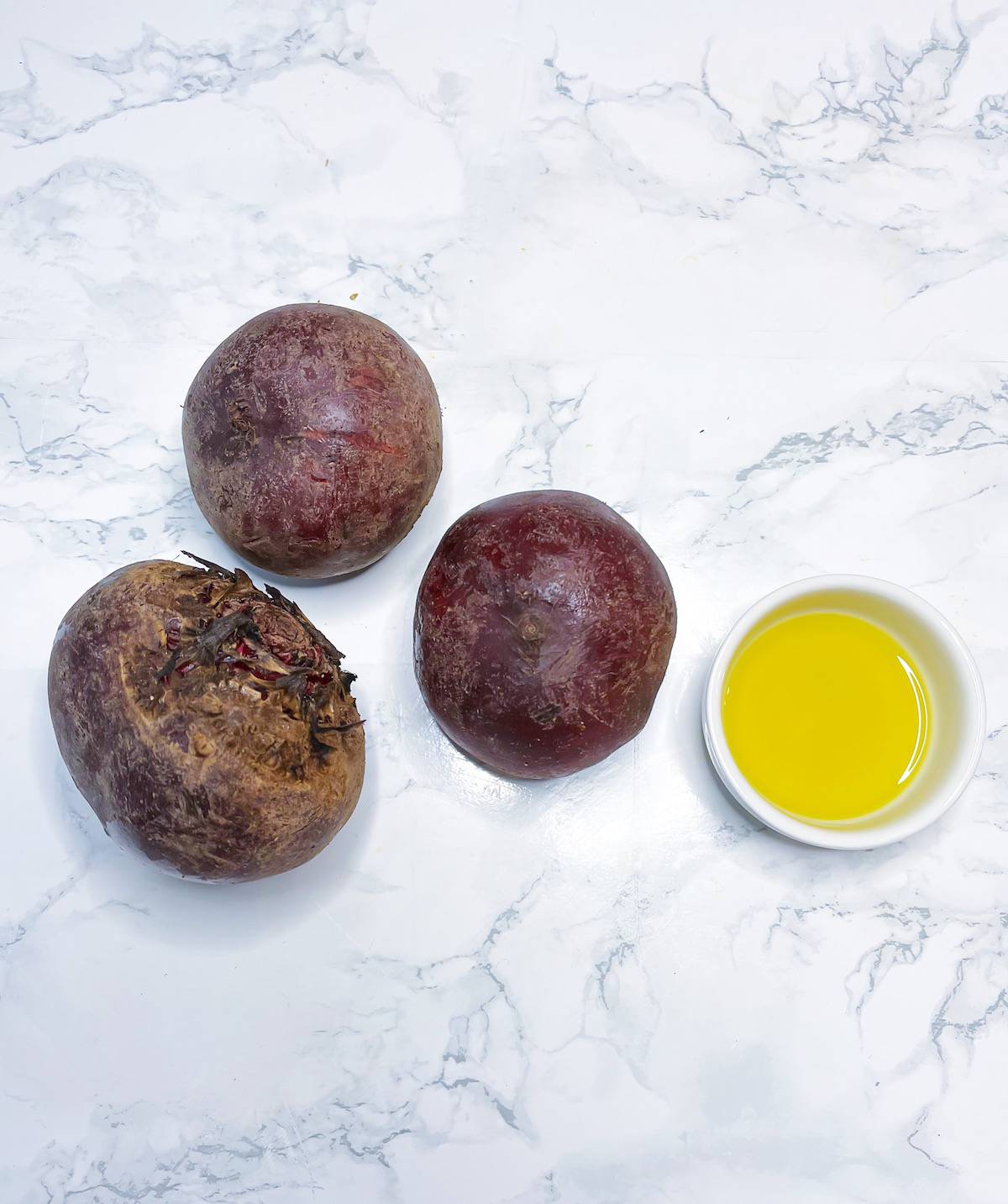 Recipe ingredients on a table including 3 large beets and a small bowl of olive oil