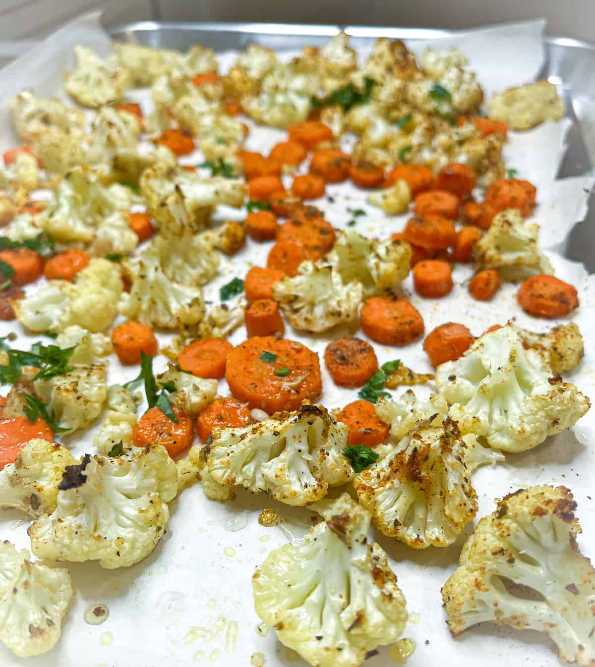 Roasted carrots and cauliflower on a baking sheet with green parsley on top