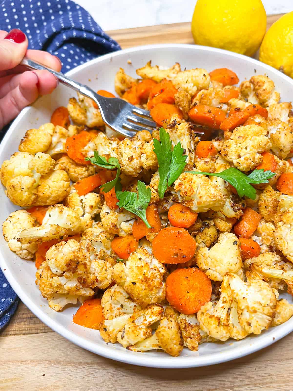 Roasted cauliflower and carrots with parsley and a hand holding a fork