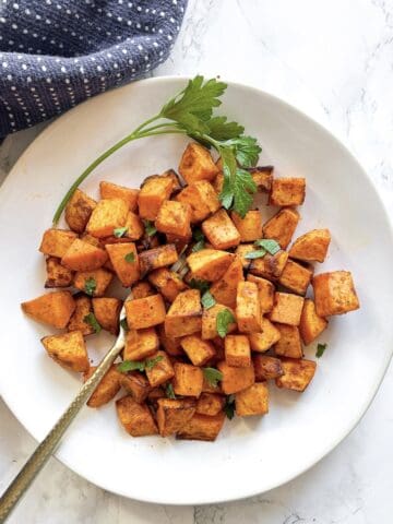air fryer sweet potato cubes with parsley garnish and fork