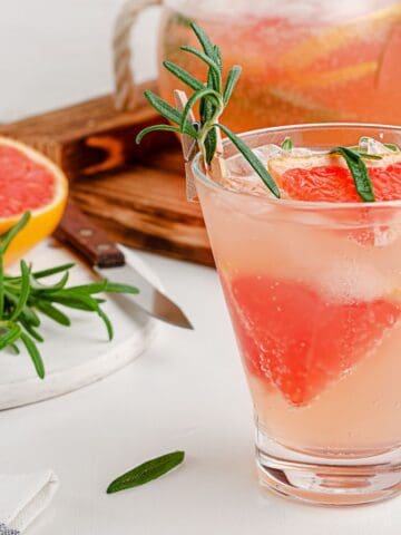 A mocktail with a slice of grapefruit and rosemary in the background