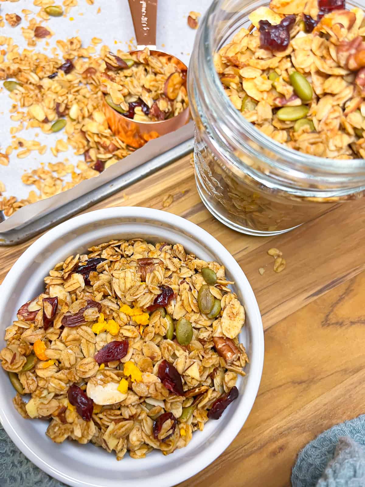 Orange granola in a mason jar and a white bowl and on a baking sheet in the background