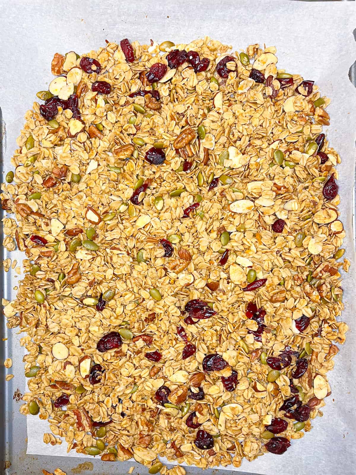 Orange granola with pecans and cranberries on a baking sheet
