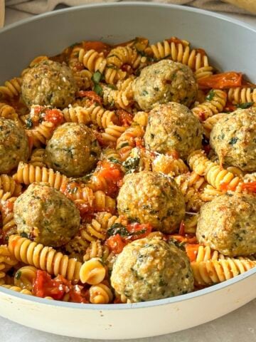 A close up of gluten free turkey meatballs with cherry tomato pasta sauce and pasta noodles.