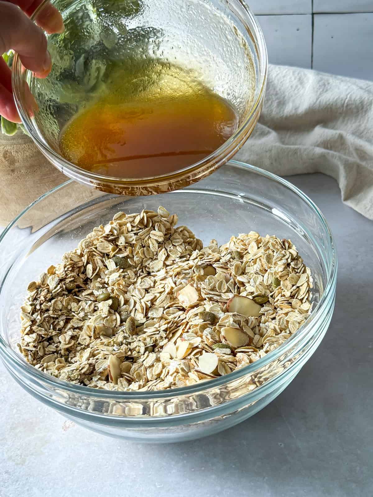 A human hand pouring wet ingredients for hemp granola into dry ingredients.