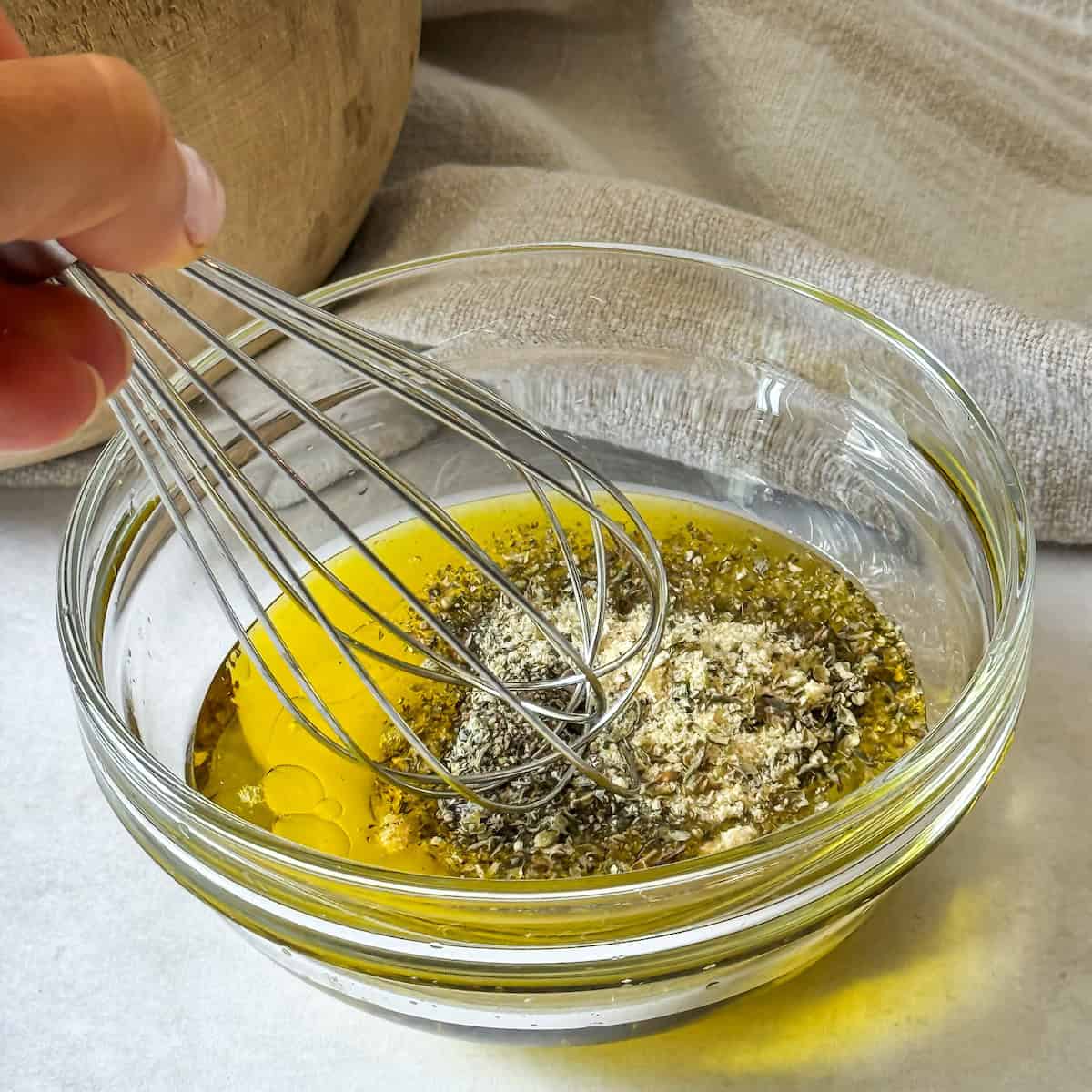 A human hand whisking marinade ingredients in a glass bowl.