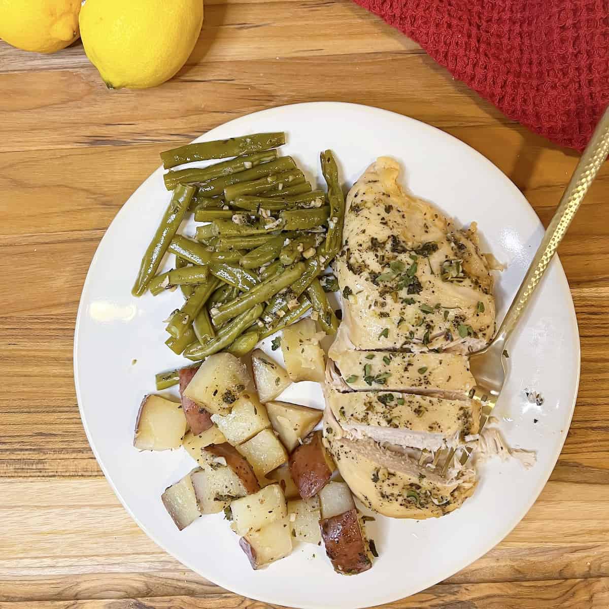 slow cooker chicken, green beans and potatoes on a white plate with fresh lemons in the background