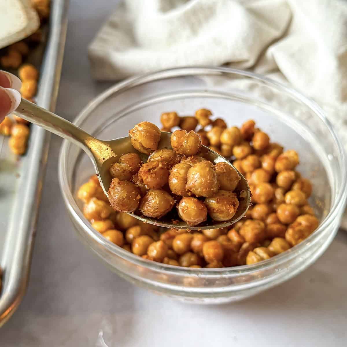 Roasted chickpeas in a glass bowl with a real human hand holding up a bite. 