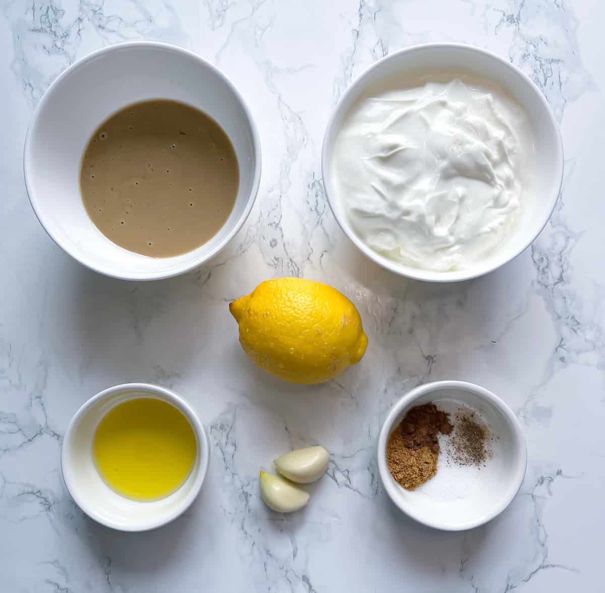 Tahini Yogurt Dip Ingredients with tahini (sesame paste), plain yogurt, extra virgin olive oil, lemon, garlic clove, and ground cumin with salt and black pepper in small bowls