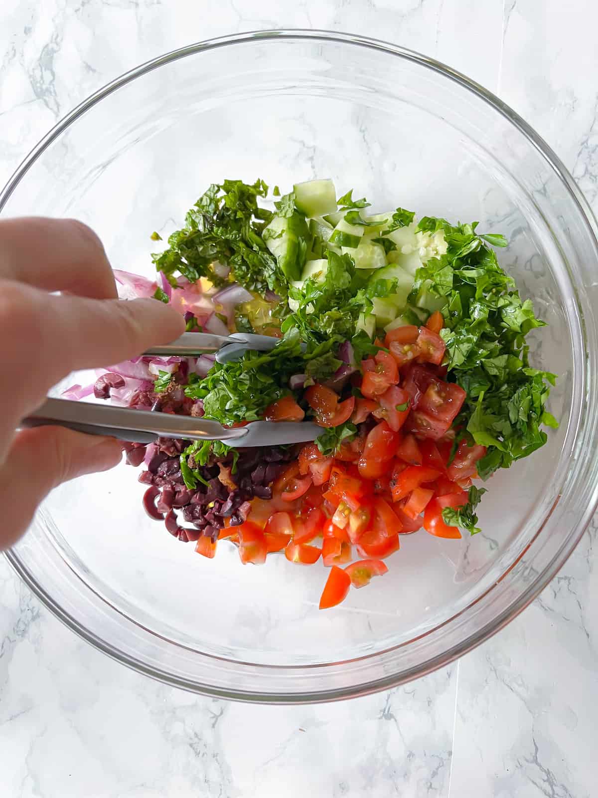 a hand mixing fresh veggies and herbs with tongs