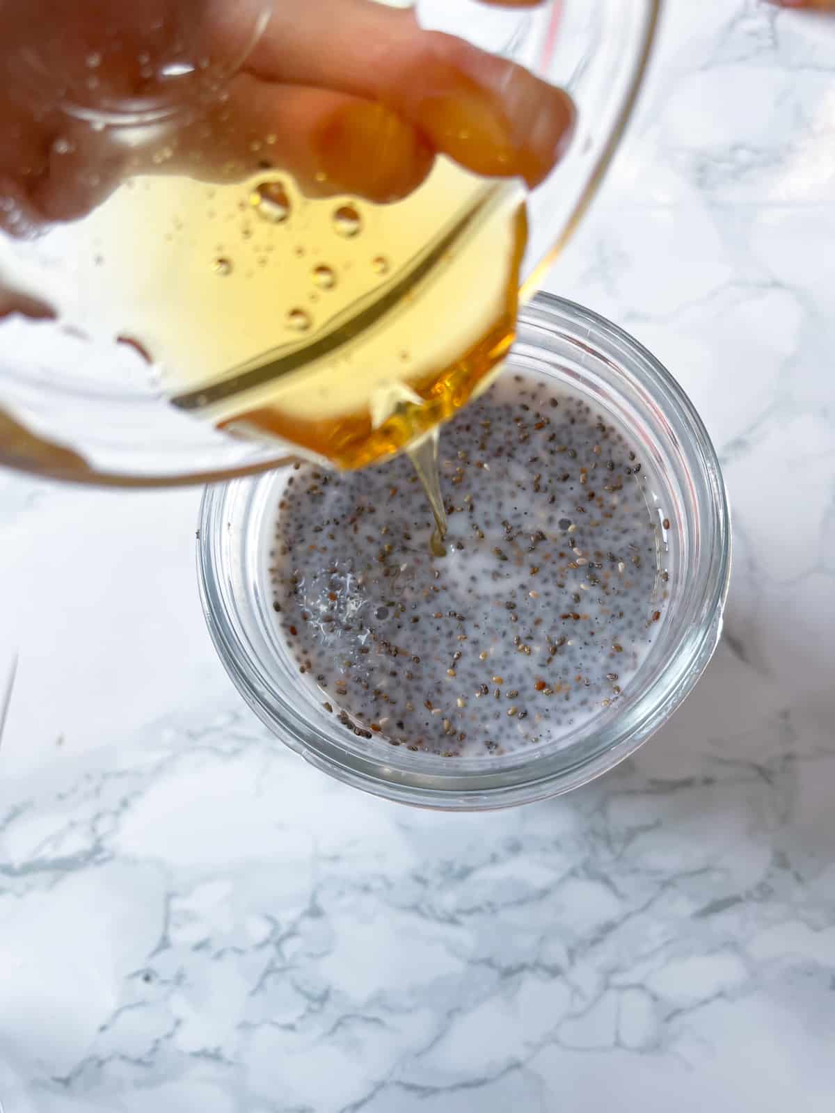 a hand pouring honey and vanilla extract into a mason jar with chia seeds and milk