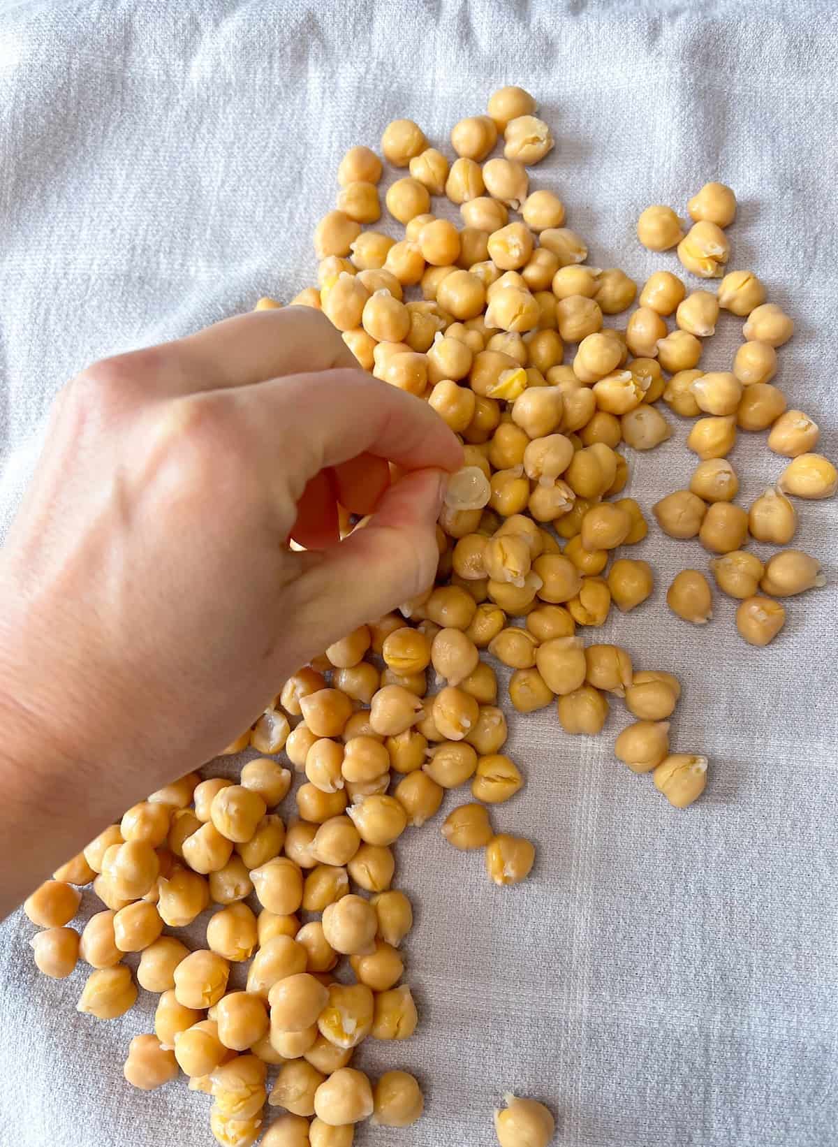 a hand taking chickpea skins off of dry chickpeas