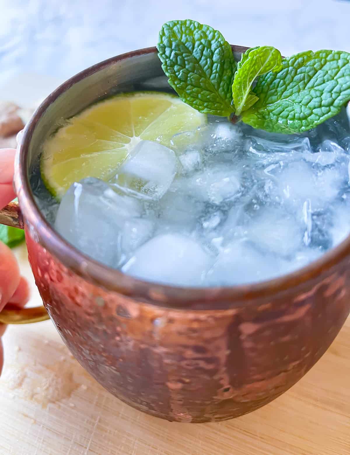 ginger beer mocktail with mint and fresh lime and a hand holding the handle on a copper mug