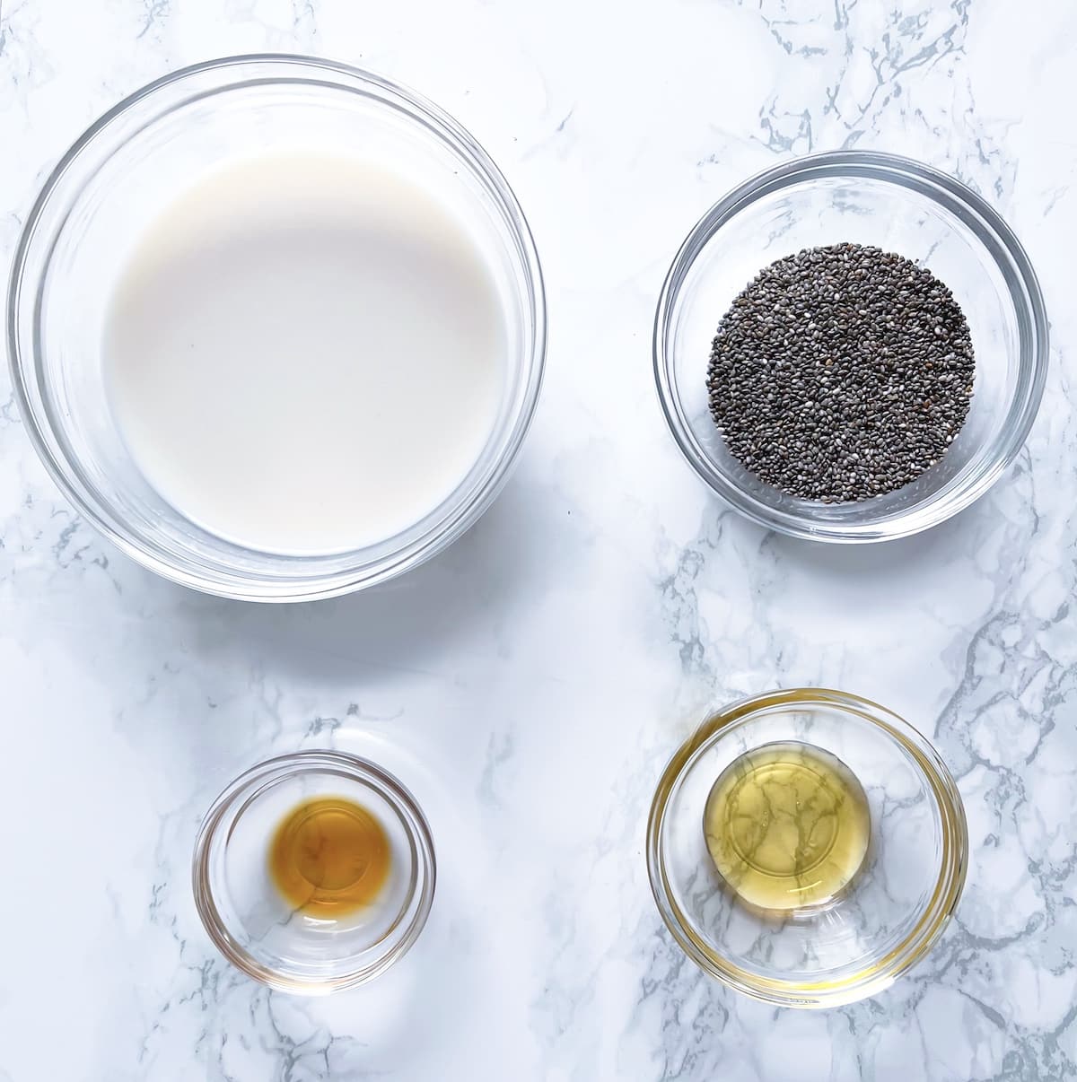 ingredients for chia seeds overnight including glass bowls with nondairy milk, chia seeds, honey, and vanilla extract on a marble table