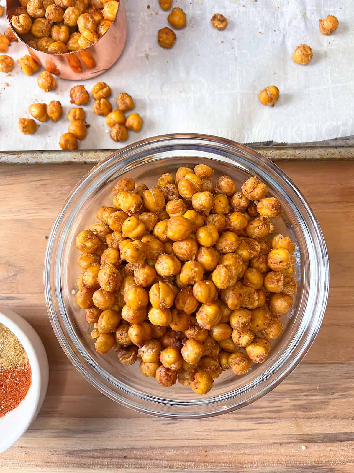 mediterranean roasted chickpeas in a glass bowl with a rimmed baking sheet in the background