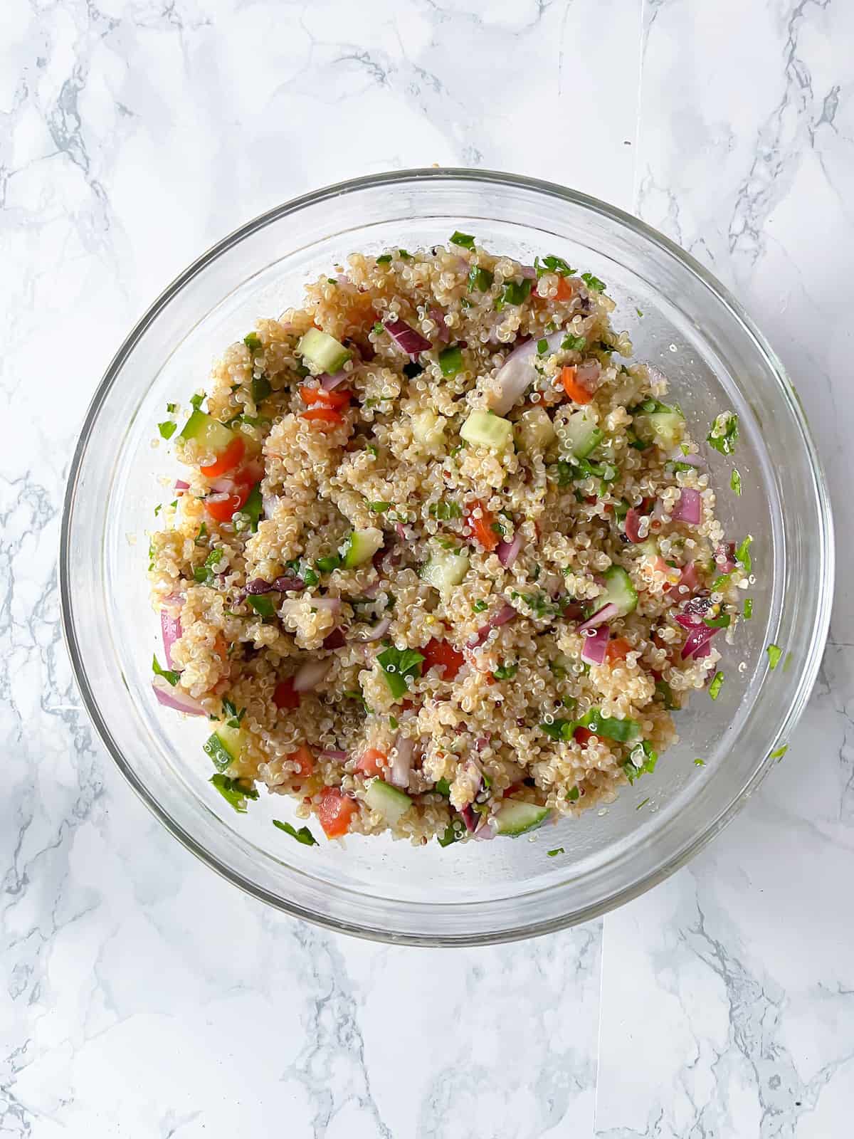 quinoa mixed with vegetables and dressing in a small glass bowl