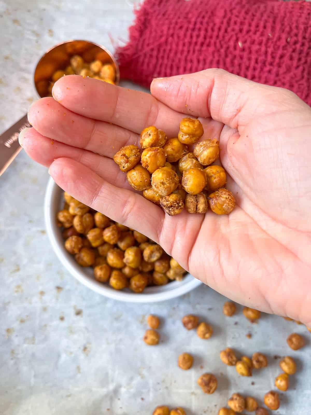 roasted chickpeas being held in a hand with a red towel in the background