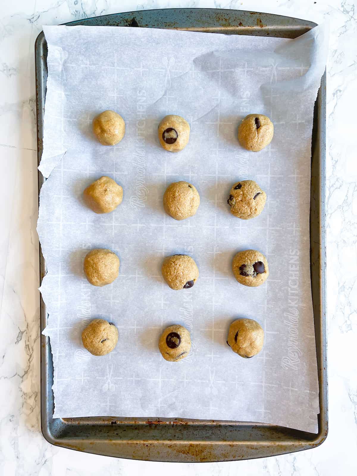 Protein cookie dough balls on a parchment-lined baking sheet from a birdseye view