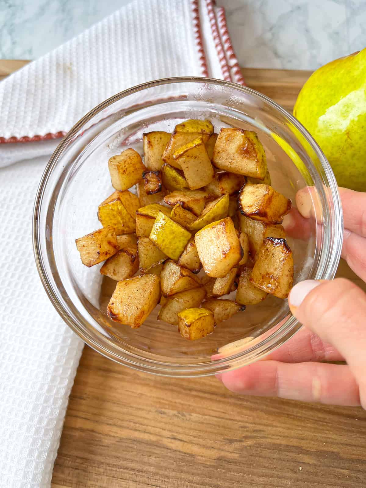 a hand holding up a bowl of air fryer pears