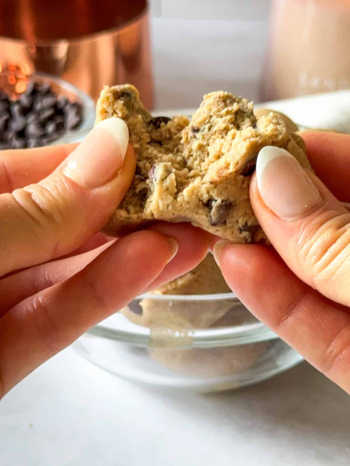 A human hand holding a protein cookie dough bite and tearing it apart to show the gooey center.