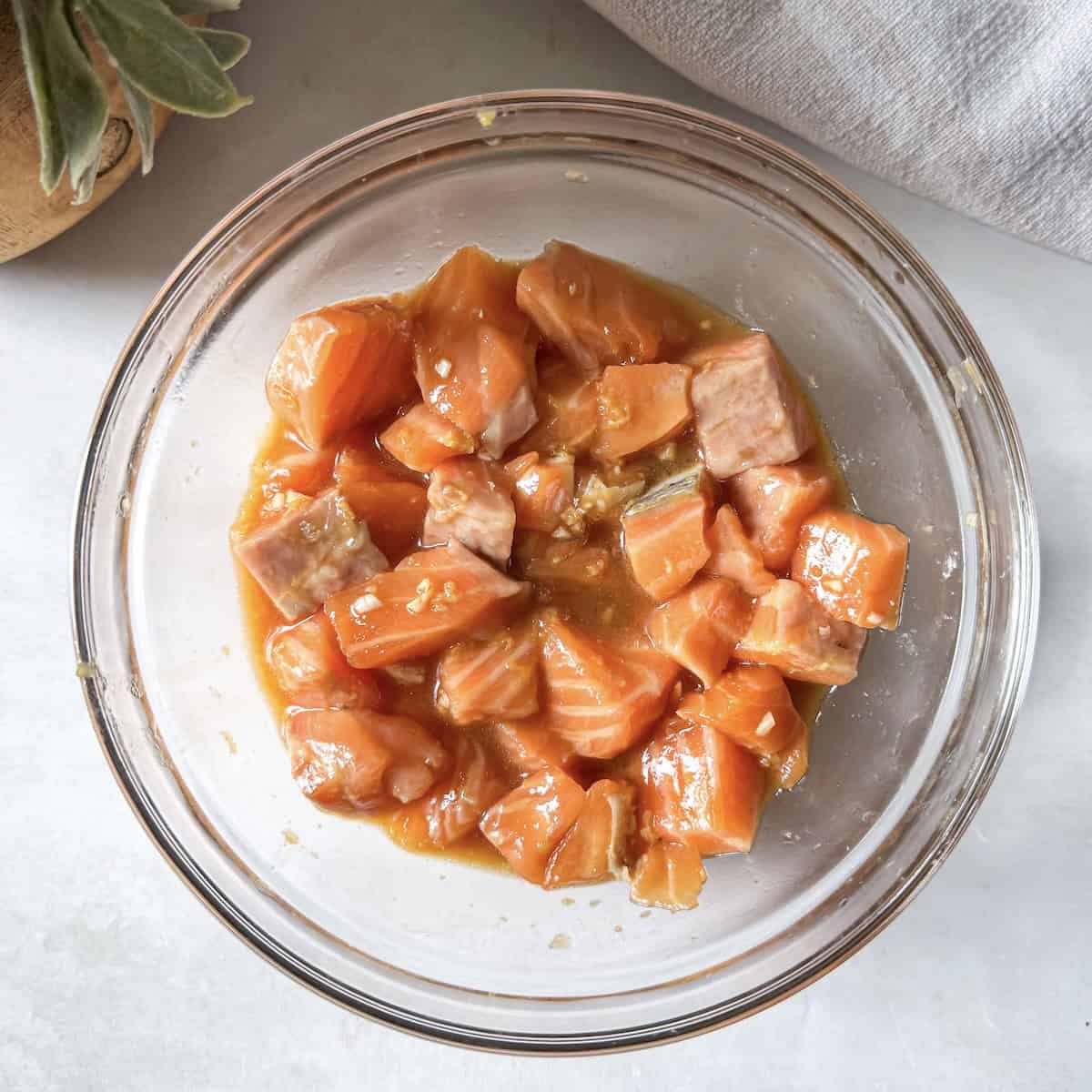cubed salmon in marinade in a glass bowl.